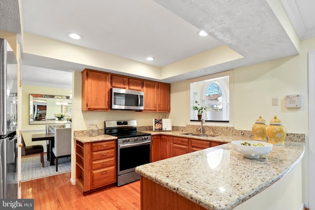 kitchen with light wood-type flooring, a sink, stainless steel appliances, a peninsula, and light stone countertops