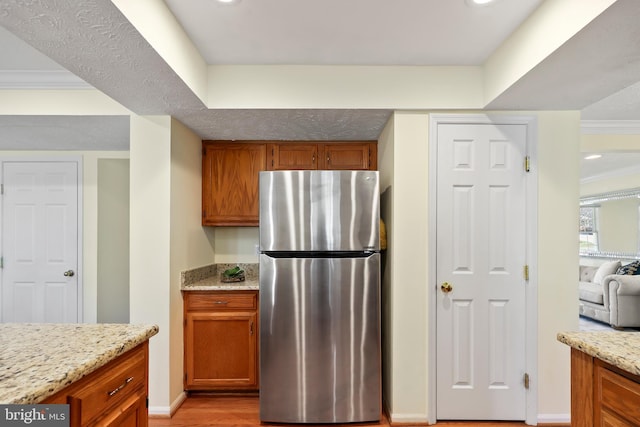 kitchen featuring brown cabinets, ornamental molding, light stone countertops, and freestanding refrigerator