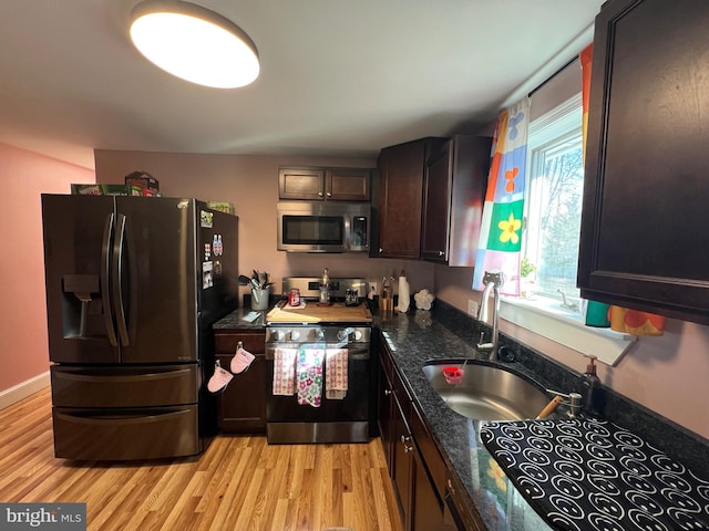 kitchen featuring dark stone countertops, a sink, dark brown cabinetry, light wood-style floors, and appliances with stainless steel finishes