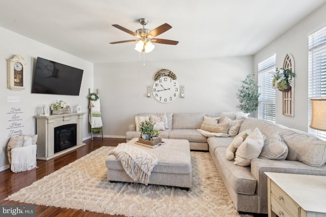 living area with a glass covered fireplace, a ceiling fan, baseboards, and wood finished floors