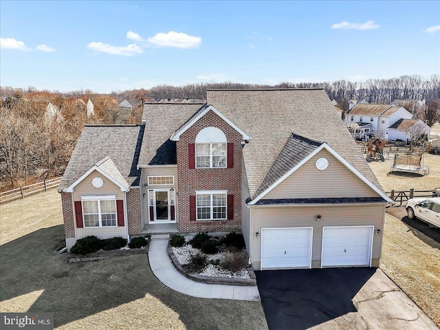 traditional-style home with brick siding, an attached garage, a front lawn, fence, and driveway