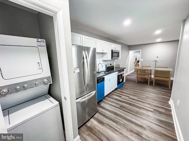 kitchen featuring stacked washer / dryer, appliances with stainless steel finishes, wood finished floors, white cabinets, and a sink