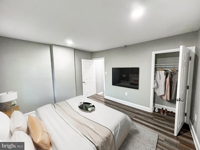 bedroom with a walk in closet, wood finished floors, a closet, and baseboards