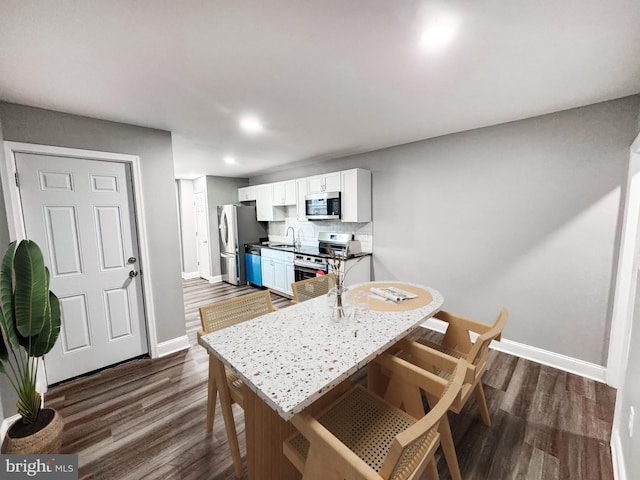 kitchen with dark wood-style floors, appliances with stainless steel finishes, white cabinets, decorative backsplash, and baseboards