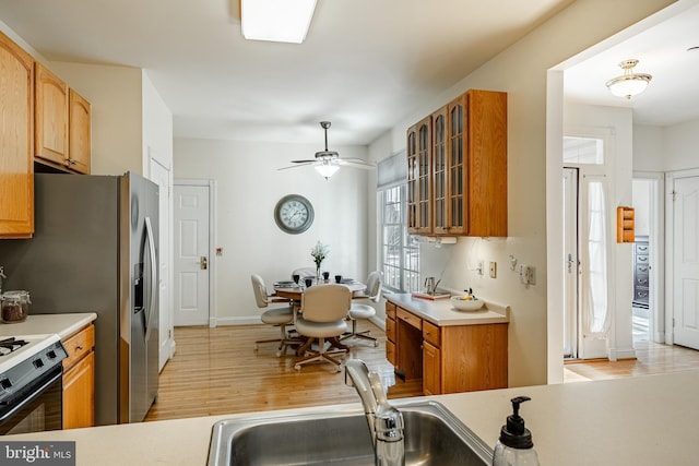 kitchen with light wood-style flooring, a sink, light countertops, glass insert cabinets, and range with gas cooktop