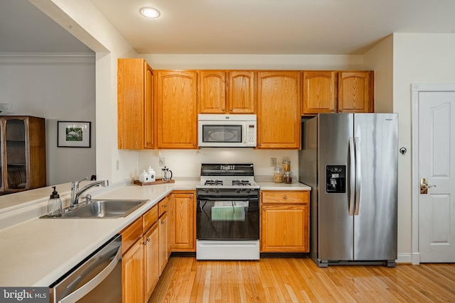 kitchen featuring appliances with stainless steel finishes, light wood-type flooring, light countertops, and a sink