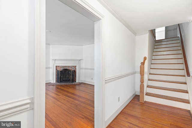 staircase with hardwood / wood-style flooring, a brick fireplace, and crown molding