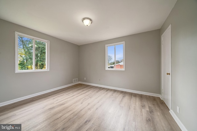 unfurnished room featuring visible vents, a healthy amount of sunlight, baseboards, and wood finished floors