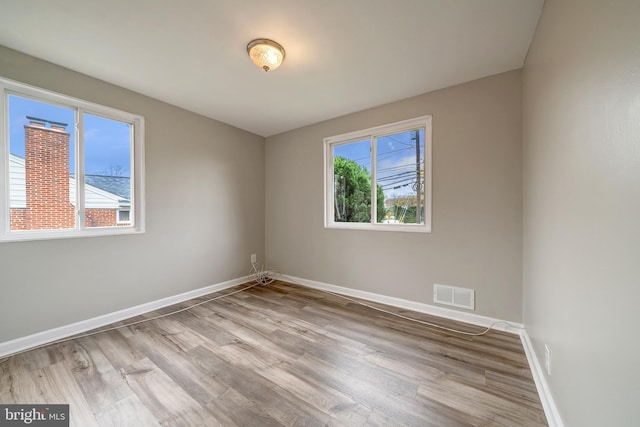 unfurnished room with plenty of natural light, visible vents, baseboards, and wood finished floors