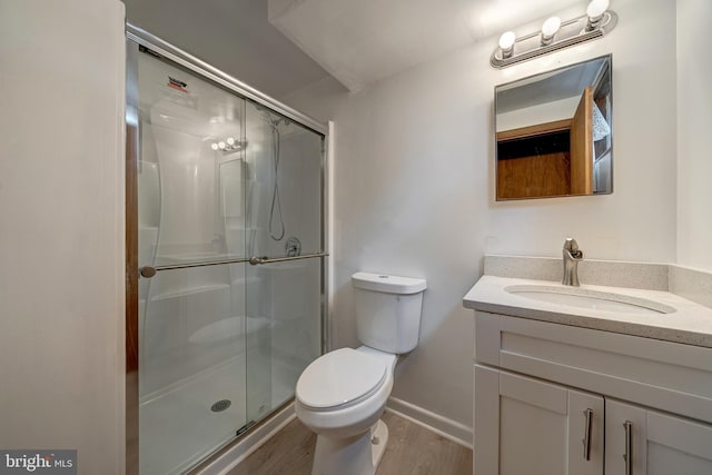 bathroom featuring toilet, a stall shower, wood finished floors, baseboards, and vanity