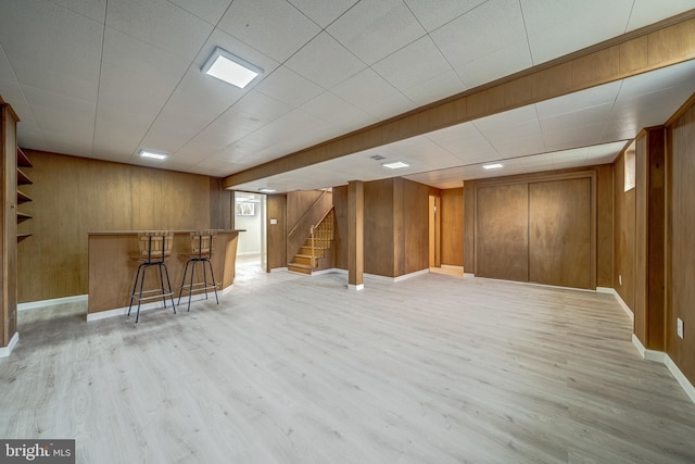 finished below grade area with a bar, light wood-style flooring, stairs, and wood walls