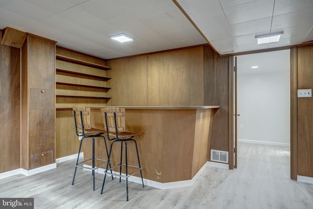 bar featuring a bar, light wood-style floors, visible vents, and wood walls