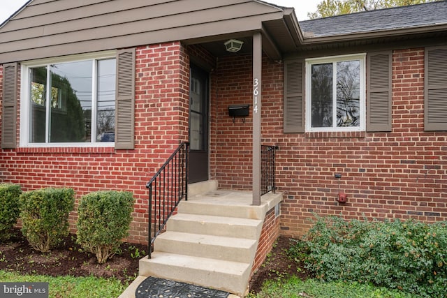 property entrance featuring brick siding and a shingled roof