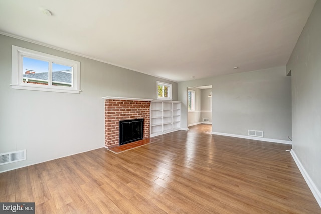 unfurnished living room with a wealth of natural light, visible vents, a brick fireplace, and wood finished floors