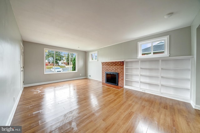 unfurnished living room with baseboards, light wood-style floors, and a brick fireplace