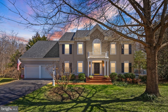 view of front of home featuring a front yard, a balcony, a shingled roof, a garage, and aphalt driveway