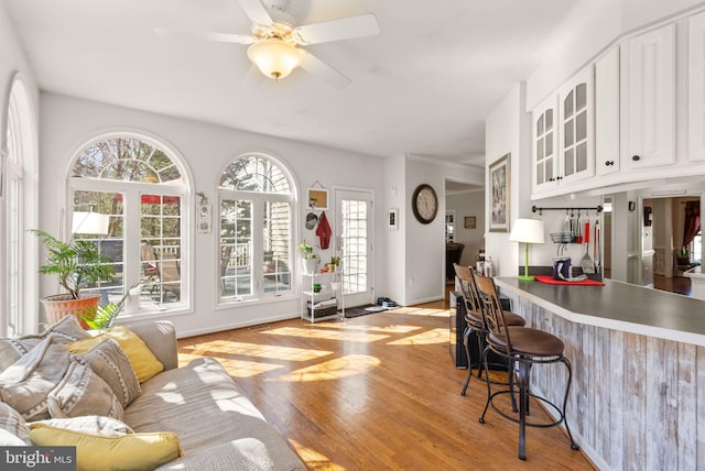 kitchen with glass insert cabinets, ceiling fan, a breakfast bar area, light wood-style flooring, and white cabinetry