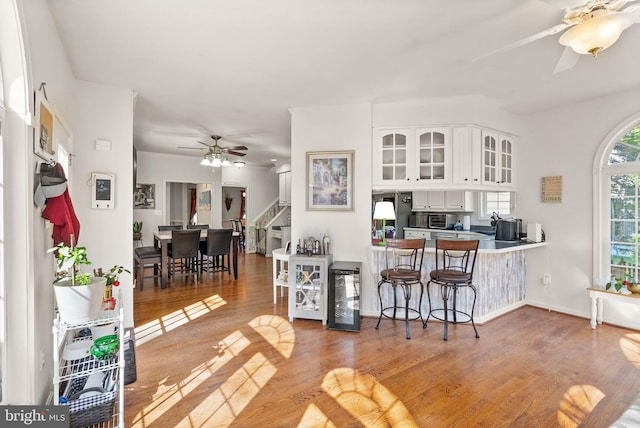 kitchen featuring a breakfast bar, beverage cooler, wood finished floors, white cabinets, and glass insert cabinets