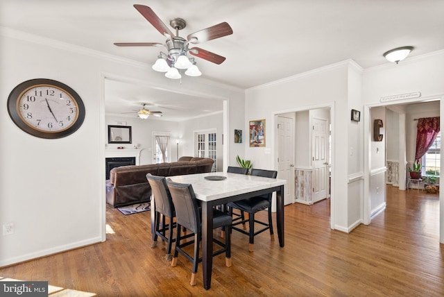 dining space featuring baseboards, wood finished floors, a fireplace, and ornamental molding