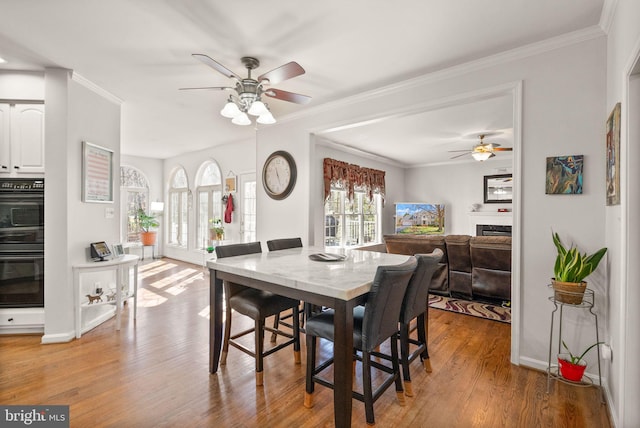 dining area with light wood-style flooring, a fireplace, baseboards, and ornamental molding