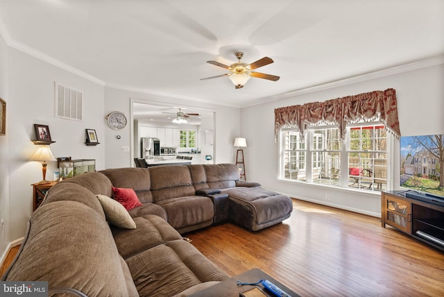 living area featuring visible vents, plenty of natural light, wood finished floors, and crown molding