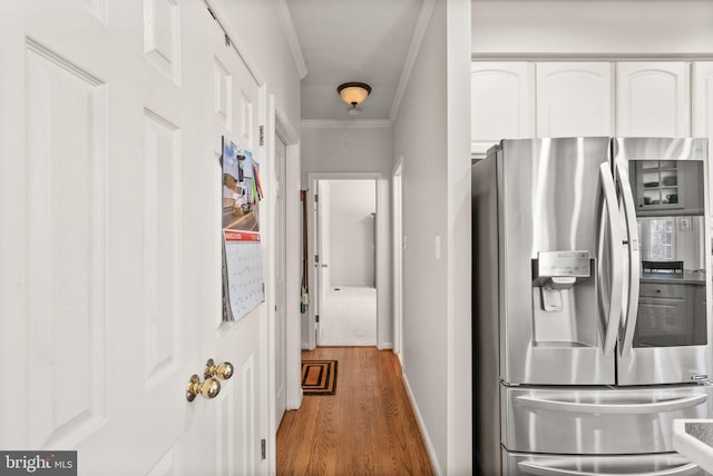 corridor featuring baseboards, light wood finished floors, and ornamental molding