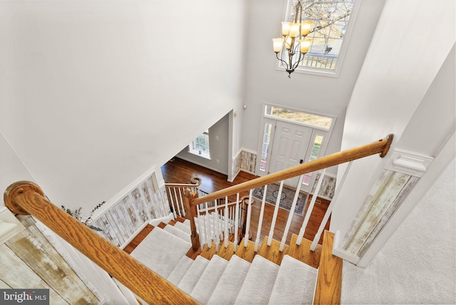 stairway featuring a notable chandelier, a high ceiling, baseboards, and wood finished floors