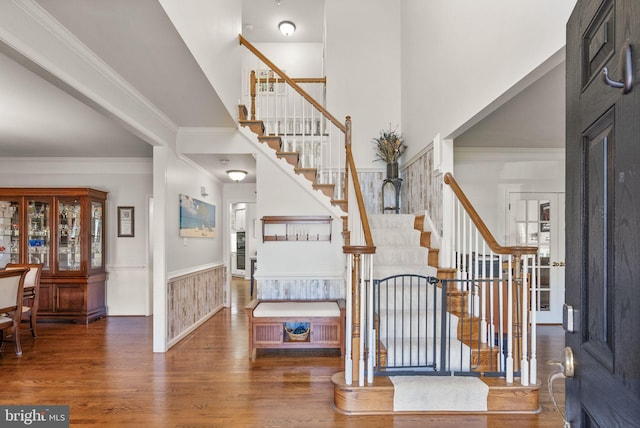 entryway with crown molding, stairs, wainscoting, a towering ceiling, and wood finished floors