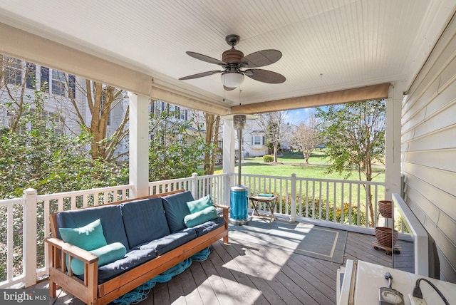 deck with outdoor lounge area, a ceiling fan, and a lawn