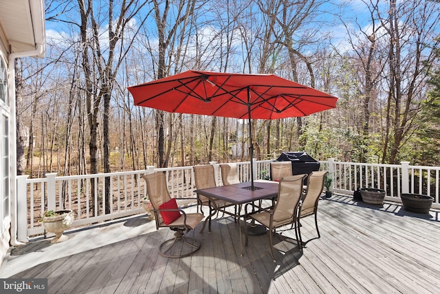 wooden deck with a grill, a view of trees, and outdoor dining area