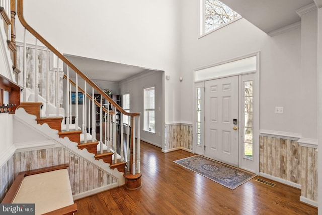 entrance foyer with a wainscoted wall, ornamental molding, visible vents, and wood finished floors