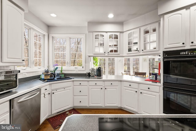 kitchen with white cabinetry, a sink, glass insert cabinets, dobule oven black, and dishwasher