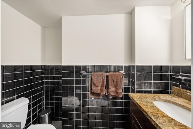 half bath featuring tile walls, toilet, vanity, and a wainscoted wall