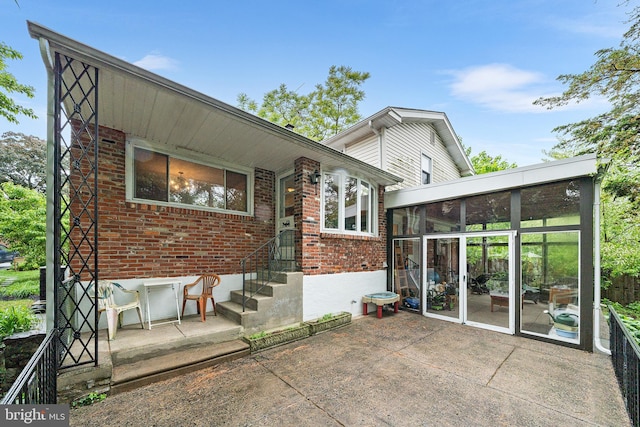rear view of house with a sunroom, brick siding, and a patio area