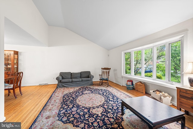 living room featuring lofted ceiling, light wood finished floors, and baseboards