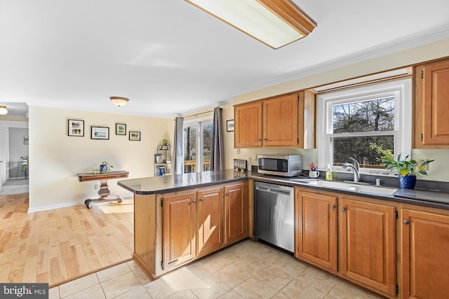 kitchen with dark countertops, brown cabinets, a peninsula, stainless steel appliances, and a sink