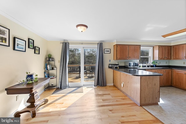 kitchen with brown cabinetry, light wood finished floors, a peninsula, ornamental molding, and dark countertops