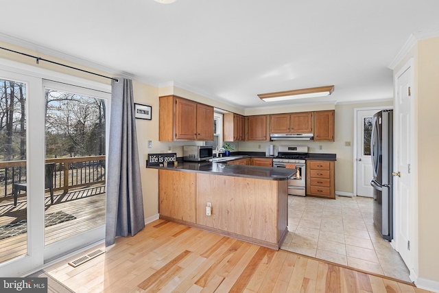 kitchen featuring dark countertops, visible vents, under cabinet range hood, appliances with stainless steel finishes, and a peninsula