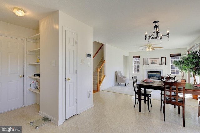 dining area with stairway, a glass covered fireplace, and ceiling fan with notable chandelier