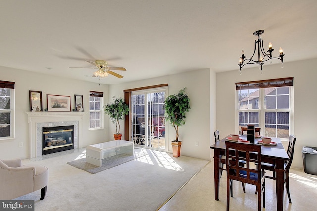 dining space featuring light colored carpet, a fireplace, and ceiling fan with notable chandelier