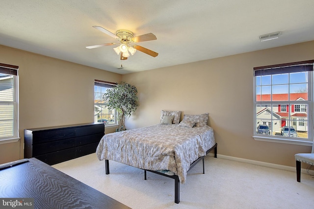 bedroom with visible vents, light colored carpet, baseboards, and ceiling fan