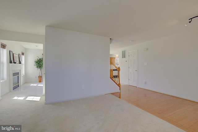 empty room featuring visible vents, stairway, a fireplace with flush hearth, carpet flooring, and wood finished floors