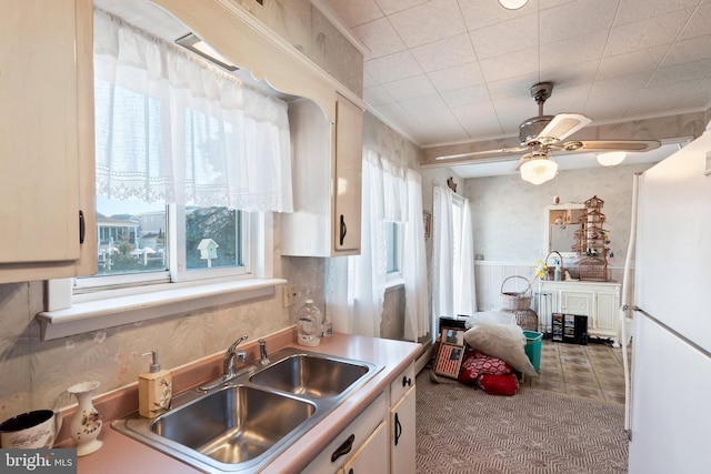 kitchen with a ceiling fan, a sink, wallpapered walls, white cabinetry, and light countertops