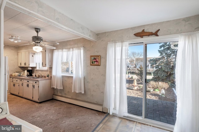 kitchen with beamed ceiling, baseboard heating, freestanding refrigerator, white cabinetry, and a sink