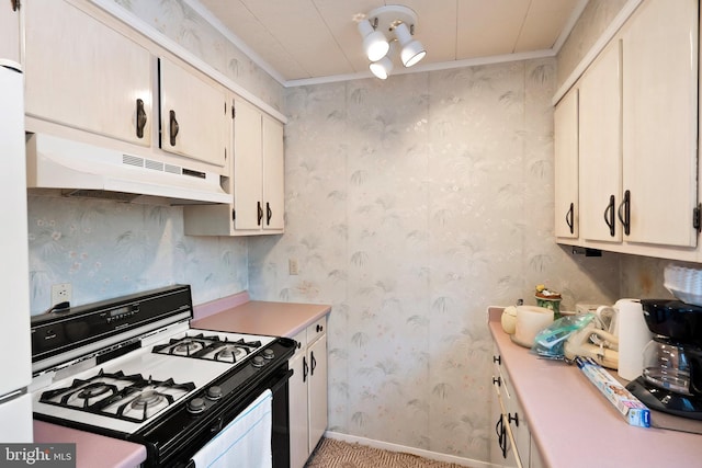 kitchen with wallpapered walls, under cabinet range hood, light countertops, ornamental molding, and gas stove