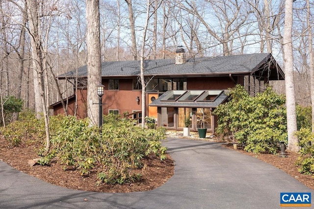 view of front of house with aphalt driveway, roof with shingles, and a chimney