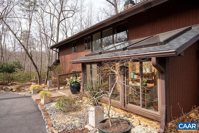 property entrance with a chimney, a wooden deck, and roof with shingles