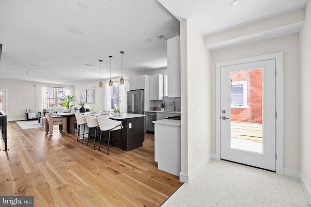 kitchen featuring white cabinetry, light countertops, appliances with stainless steel finishes, a kitchen bar, and a center island