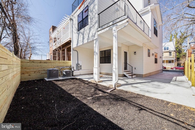 view of side of home with fence, entry steps, central AC unit, a balcony, and a patio