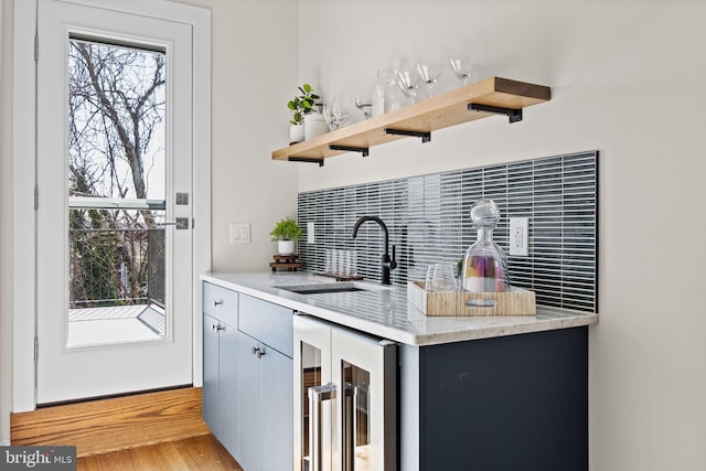 kitchen with light wood-style flooring, beverage cooler, open shelves, a sink, and tasteful backsplash